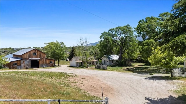 view of front facade with dirt driveway, a garage, a barn, an outdoor structure, and a mountain view