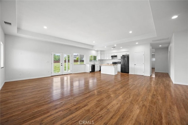 unfurnished living room with a tray ceiling, recessed lighting, baseboards, and dark wood finished floors