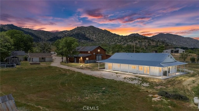 back of property at dusk featuring driveway, a mountain view, an outbuilding, a storage unit, and a yard