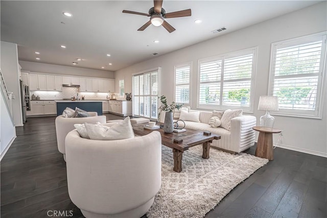 living area with plenty of natural light, a ceiling fan, dark wood-style floors, baseboards, and recessed lighting