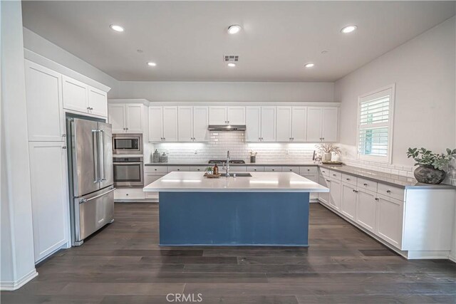 kitchen featuring appliances with stainless steel finishes, white cabinetry, tasteful backsplash, a kitchen island with sink, and light countertops