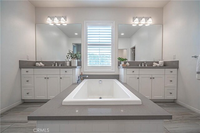 bathroom with a tub to relax in, baseboards, two vanities, and recessed lighting