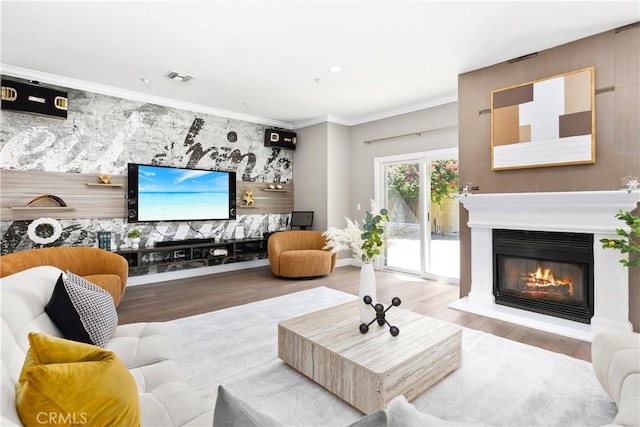 living area with a glass covered fireplace, wood finished floors, and crown molding