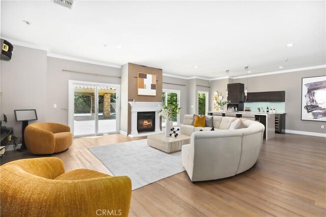 living room with light wood-style floors, recessed lighting, a lit fireplace, bar area, and baseboards