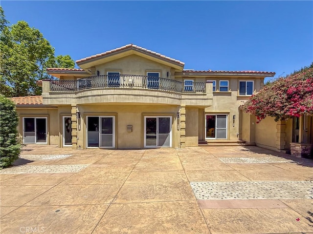 back of property featuring a balcony, a tile roof, a patio, and stucco siding
