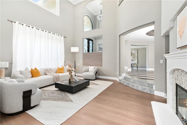 living room featuring a glass covered fireplace, wood finished floors, arched walkways, baseboards, and a high ceiling