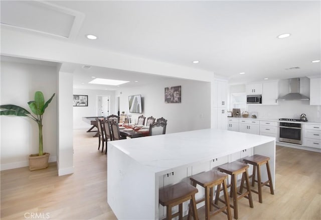 12842 Elizabeth Way, Tustin, CA 92780 - kitchen with wall chimney exhaust hood, stainless steel appliances, a center island, a breakfast bar area, and white cabinets
