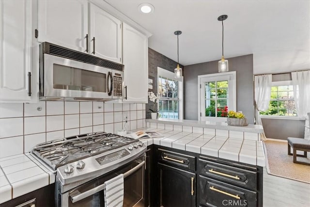3061 Wood Dr, Cambria, CA 93428 - kitchen with stainless steel appliances, white cabinets, a peninsula, tile counters, and dark cabinets