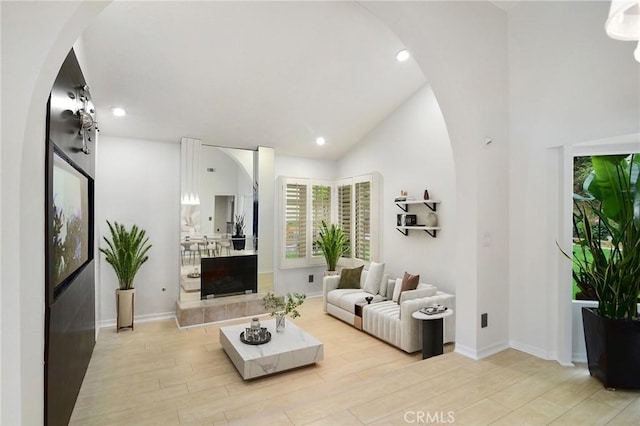 living area with lofted ceiling, arched walkways, light wood-type flooring, recessed lighting, and baseboards