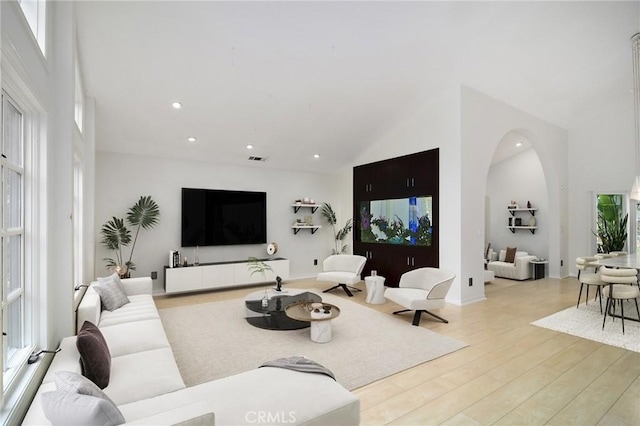 living room featuring recessed lighting, wood finished floors, arched walkways, and high vaulted ceiling