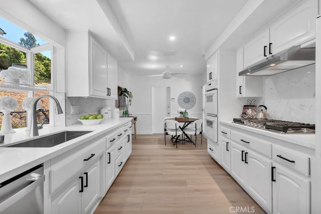 kitchen featuring appliances with stainless steel finishes, under cabinet range hood, a sink, decorative backsplash, and recessed lighting