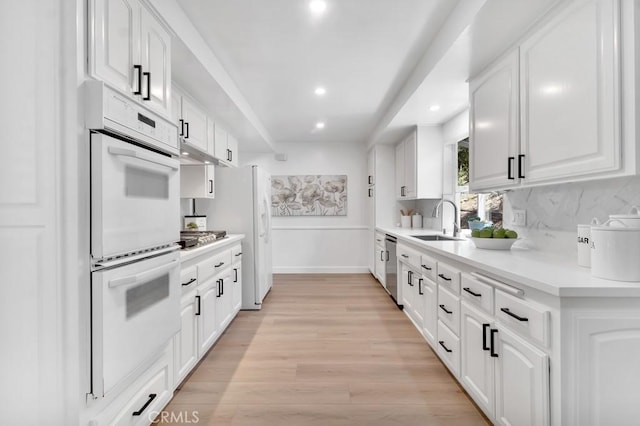 kitchen featuring white appliances, a sink, white cabinets, light countertops, and recessed lighting