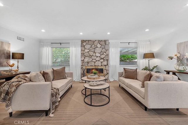 living area featuring ornamental molding, plenty of natural light, wood finished floors, recessed lighting, and a stone fireplace