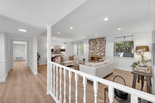living room with light wood-type flooring, a stone fireplace, baseboards, and recessed lighting