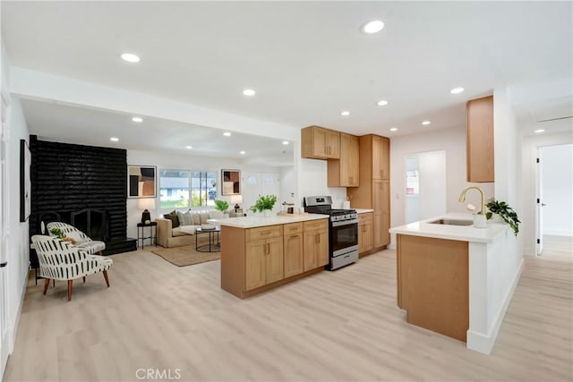 kitchen featuring stainless steel range with gas stovetop, a sink, light brown cabinets, a peninsula, and light wood-type flooring