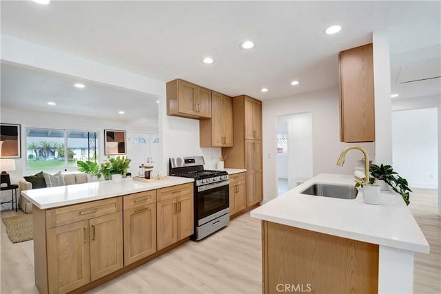 kitchen featuring stainless steel range with gas cooktop, a sink, a peninsula, light wood-style floors, and light countertops