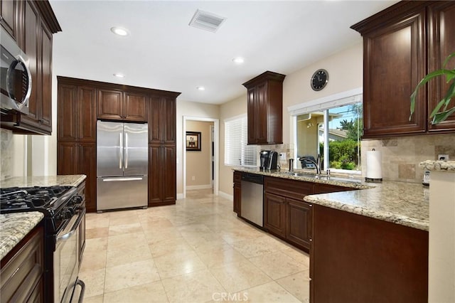kitchen featuring stainless steel appliances, tasteful backsplash, light stone counters, baseboards, and a sink