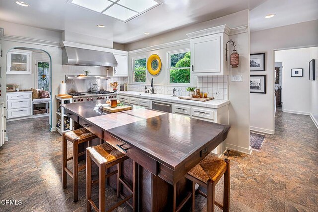 2707 Hermosita Dr, Glendale, CA 91208 - kitchen featuring dark stone finish floors, wall chimney exhaust hood, white cabinets, tasteful backsplash, and stainless steel dishwasher