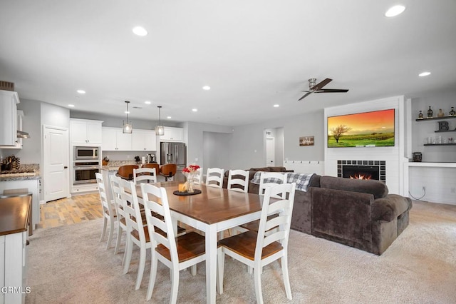 dining space featuring recessed lighting, a ceiling fan, a tiled fireplace, and light wood-style floors