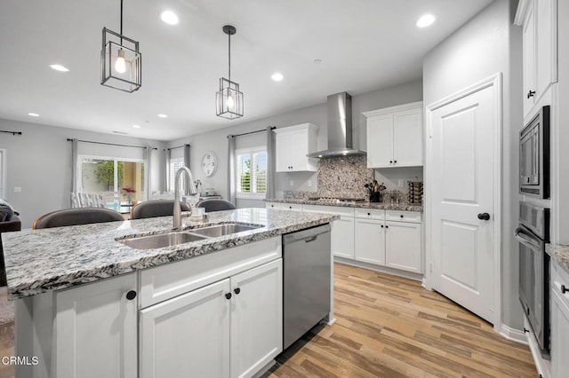 kitchen featuring wall chimney exhaust hood, a sink, stainless steel appliances, light wood-style floors, and white cabinets