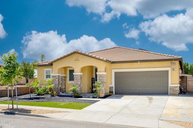 mediterranean / spanish house with stone siding, stucco siding, a garage, driveway, and fence