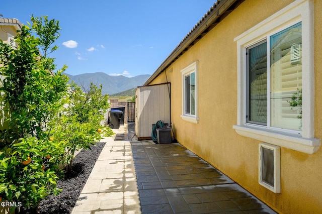 view of side of property featuring stucco siding, a mountain view, a patio, and fence