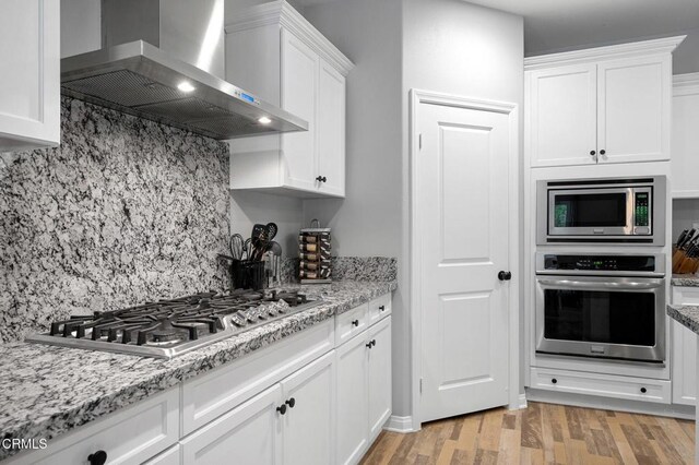 17837 Grapevine Ln, San Bernardino, CA 92407 - kitchen featuring appliances with stainless steel finishes, wall chimney range hood, white cabinets, backsplash, and light wood finished floors