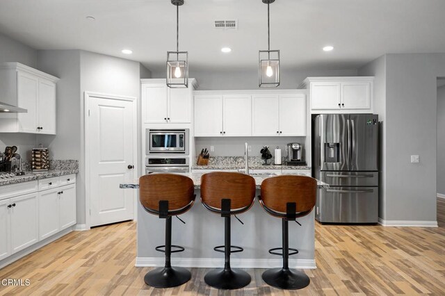 17837 Grapevine Ln, San Bernardino, CA 92407 - kitchen with appliances with stainless steel finishes, light wood finished floors, white cabinets, a center island with sink, and light stone counters