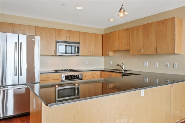 kitchen with appliances with stainless steel finishes, a sink, a peninsula, dark stone counters, and recessed lighting