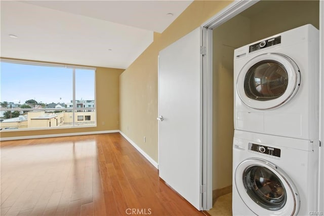 washroom featuring estacked washer and dryer, baseboards, and light wood-style flooring