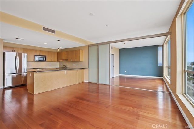 kitchen with appliances with stainless steel finishes, open floor plan, a sink, a peninsula, and wood finished floors
