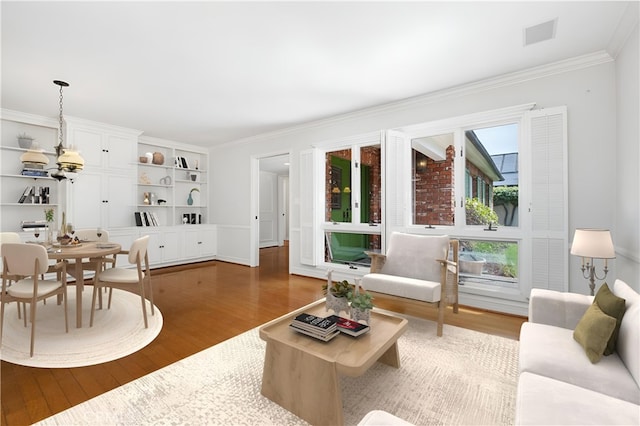 living area with wood finished floors, healthy amount of natural light, crown molding, and built in shelves