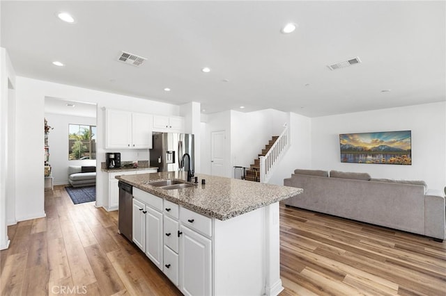 kitchen with stainless steel appliances, a sink, light wood-style flooring, a kitchen island with sink, and white cabinets