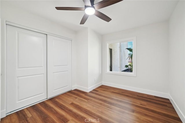 unfurnished bedroom featuring baseboards, a closet, wood finished floors, and a ceiling fan