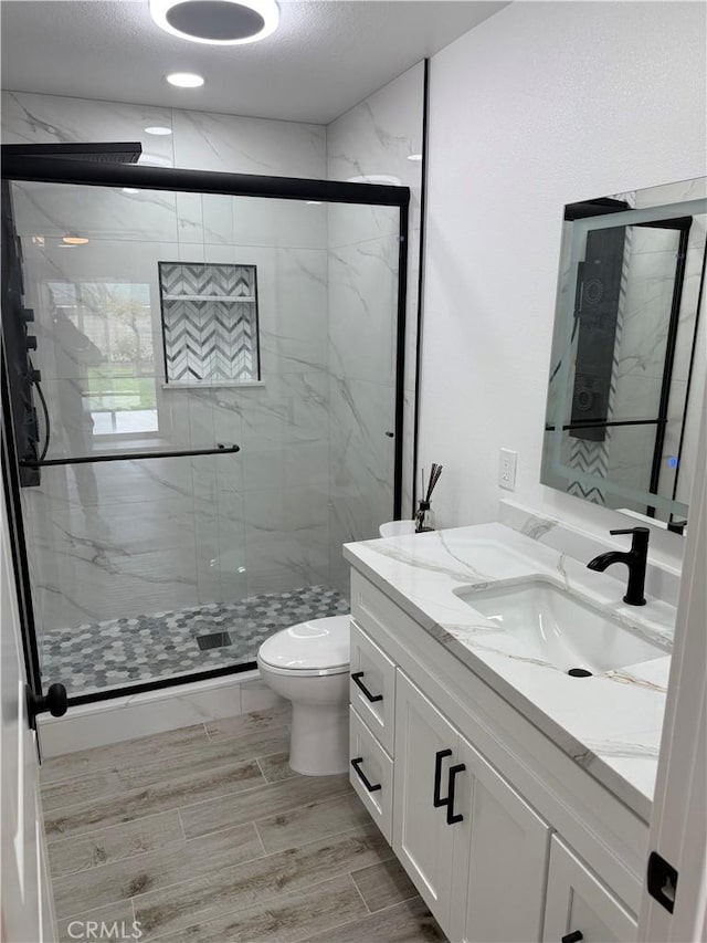 bathroom with a marble finish shower, toilet, and vanity