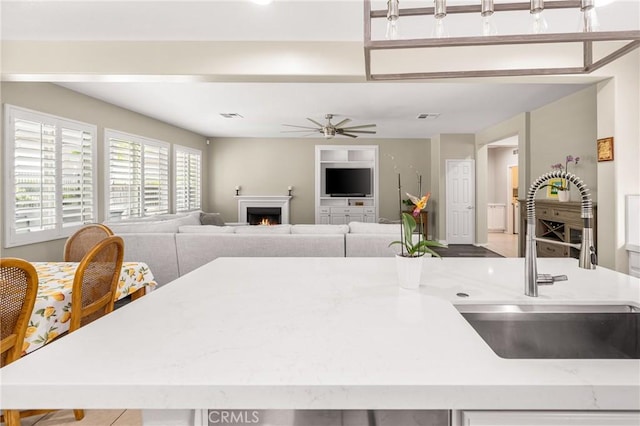 32748 Stonefield Ln, Temecula, CA 92592 - kitchen featuring a sink, ceiling fan, light stone counters, a lit fireplace, and open floor plan