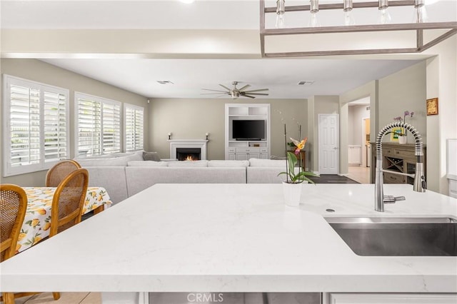 32748 Stonefield Ln, Temecula, CA 92592 - kitchen with a sink, a ceiling fan, light stone countertops, a lit fireplace, and open floor plan