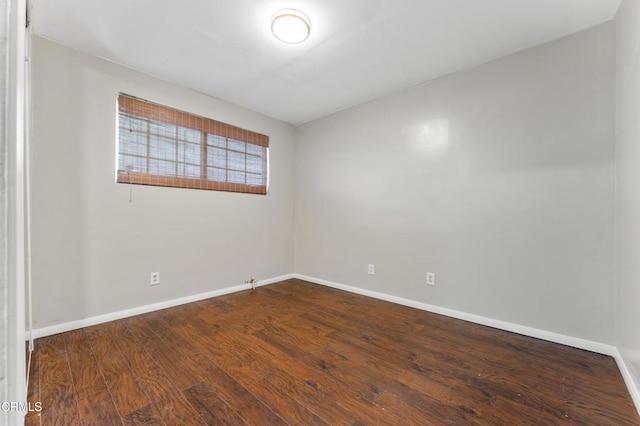 empty room featuring baseboards and dark wood-type flooring