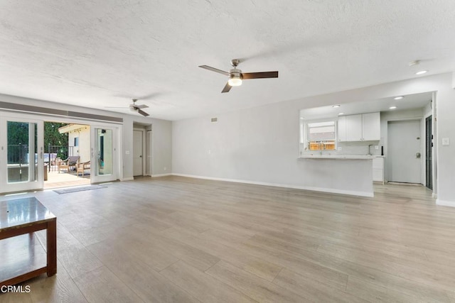 unfurnished living room featuring a textured ceiling, baseboards, a ceiling fan, light wood-style floors, and recessed lighting
