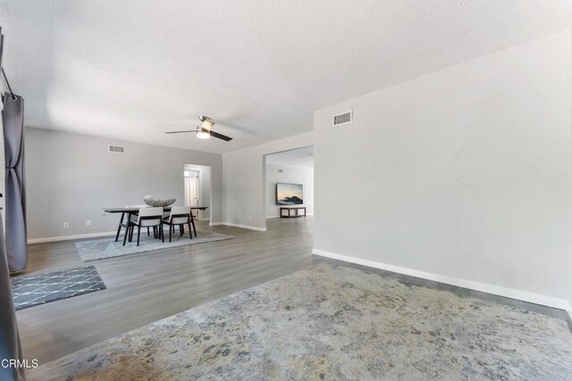 living area featuring a ceiling fan, wood finished floors, baseboards, and a textured ceiling