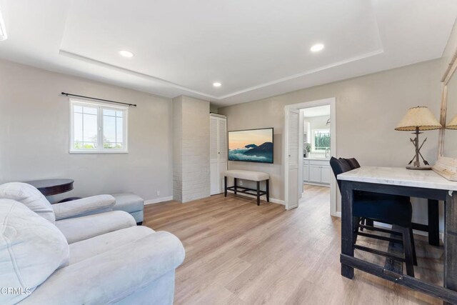 living room featuring a raised ceiling, light wood-style flooring, baseboards, and recessed lighting