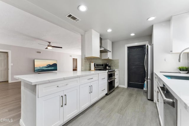 8534 Beverly Dr, San Gabriel, CA 91775 - kitchen featuring appliances with stainless steel finishes, wall chimney range hood, a peninsula, light wood-style floors, and white cabinetry