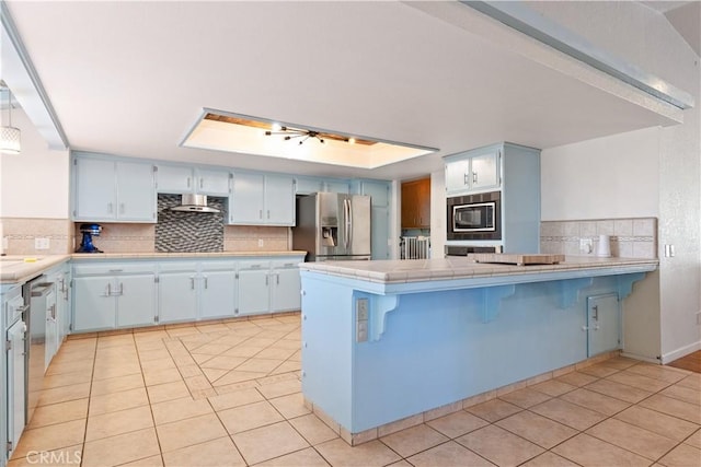 kitchen featuring stainless steel fridge, built in microwave, a peninsula, and light tile patterned flooring