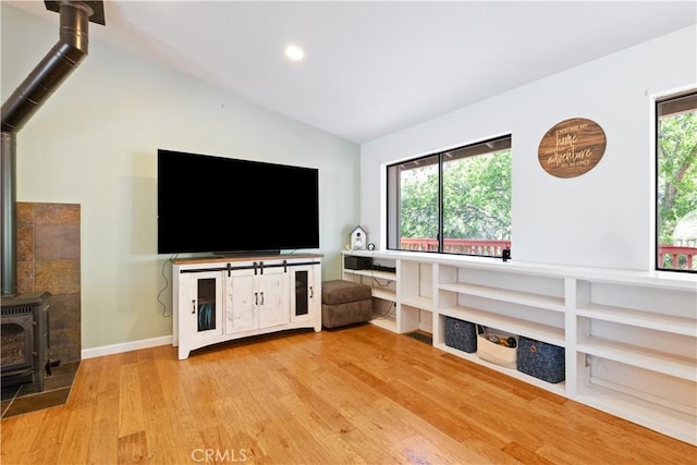 unfurnished living room with a wood stove, light wood finished floors, lofted ceiling, baseboards, and recessed lighting