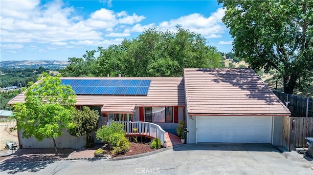 view of front facade featuring roof mounted solar panels, asphalt driveway, an attached garage, and fence