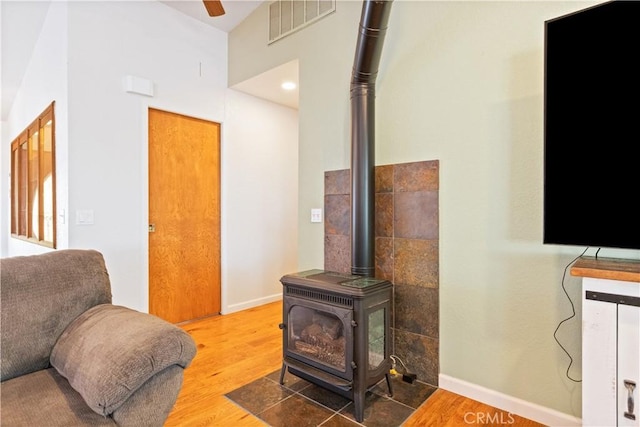 living area with a wood stove, wood finished floors, baseboards, and ceiling fan