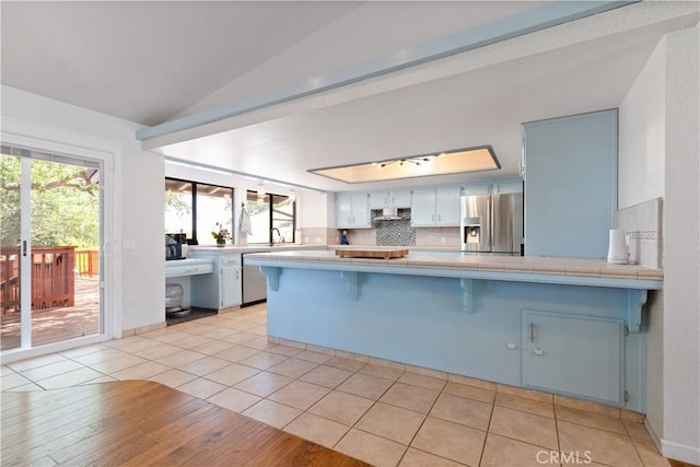 kitchen featuring stainless steel appliances, a peninsula, tile counters, healthy amount of natural light, and lofted ceiling