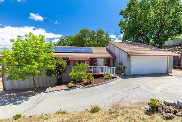 ranch-style home with roof mounted solar panels, an attached garage, asphalt driveway, and a tile roof