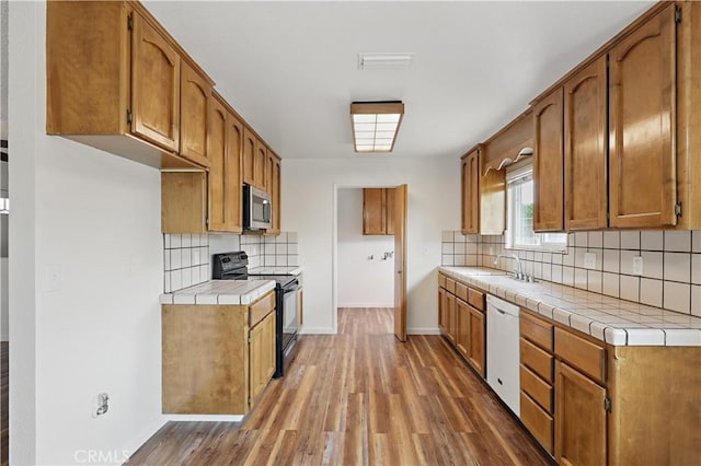 kitchen featuring electric range, white dishwasher, tile counters, stainless steel microwave, and light wood-style flooring
