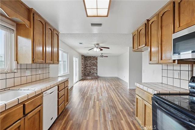 kitchen featuring tile counters, stainless steel microwave, black electric range, white dishwasher, and a ceiling fan